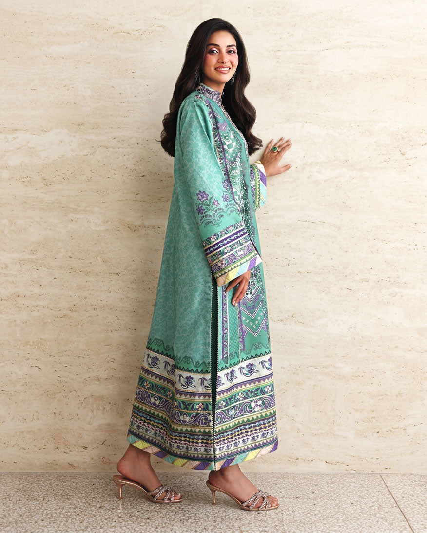 Side view of green printed raw silk suit walking, showing embroidered hem border