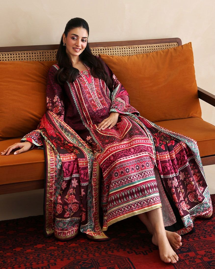 Woman wearing deep purple printed raw silk suit seated on a sofa with dupatta pooling on floor