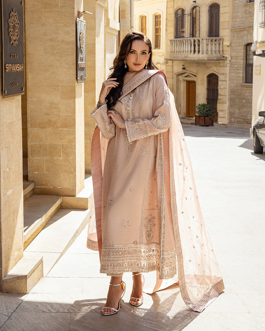Woman wearing rose beige raw silk suit with organza dupatta draped over shoulder on sunlit street
