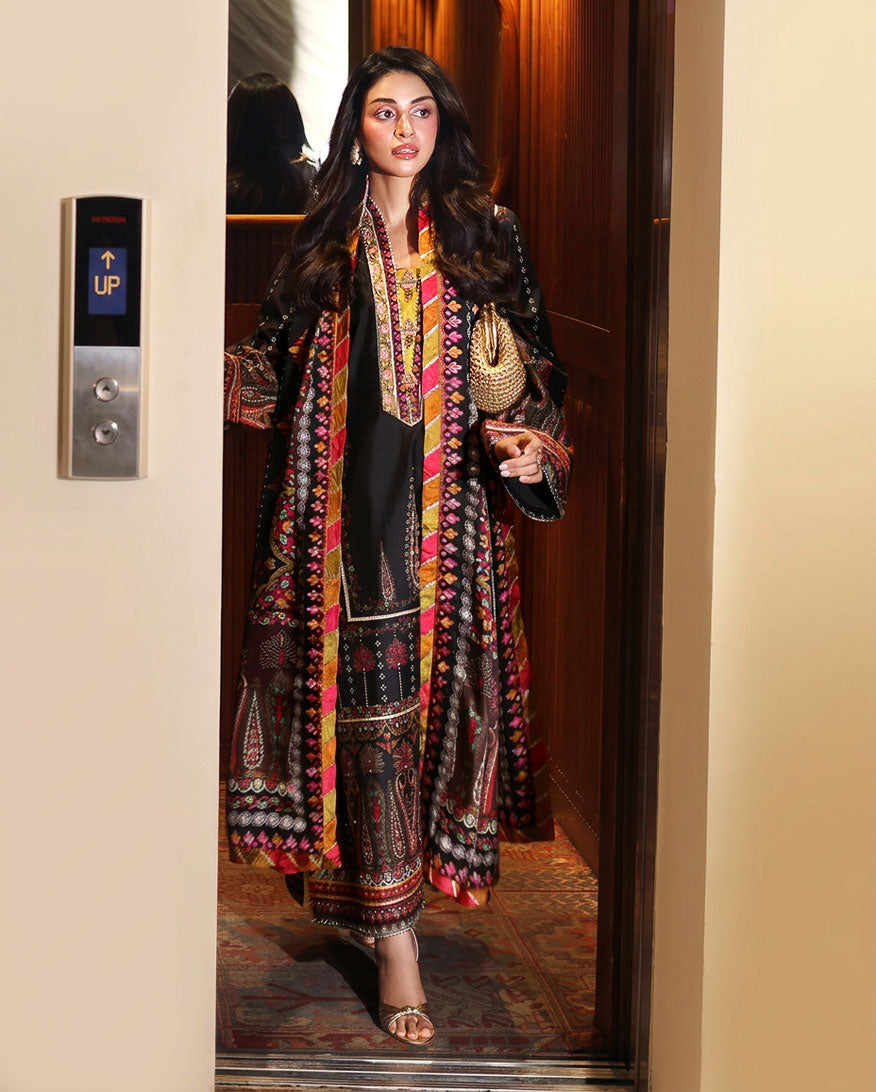 Woman wearing black printed raw silk suit standing in an elevator doorway holding a gold clutch