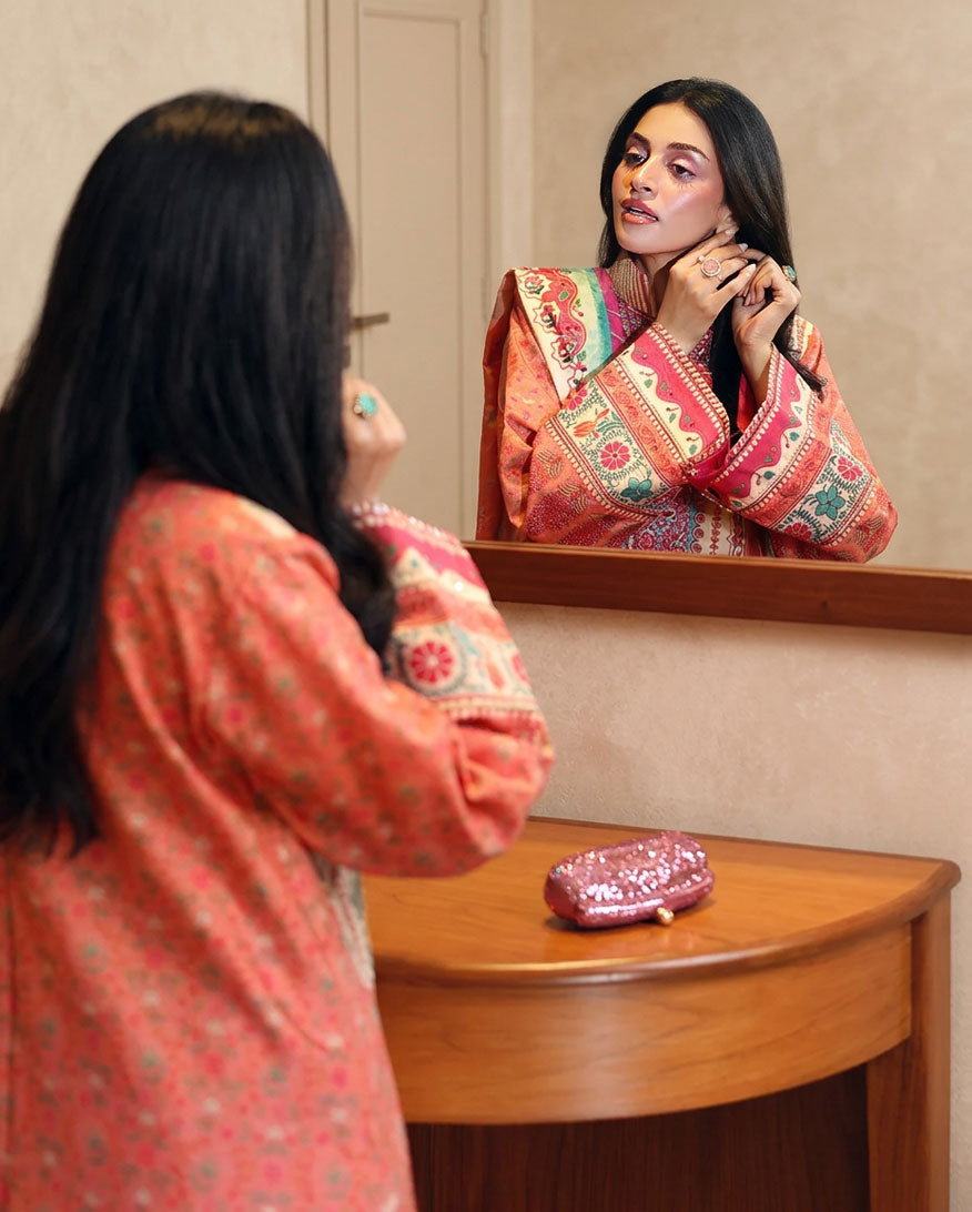 Woman wearing peach printed raw silk suit adjusting earring in front of a mirror