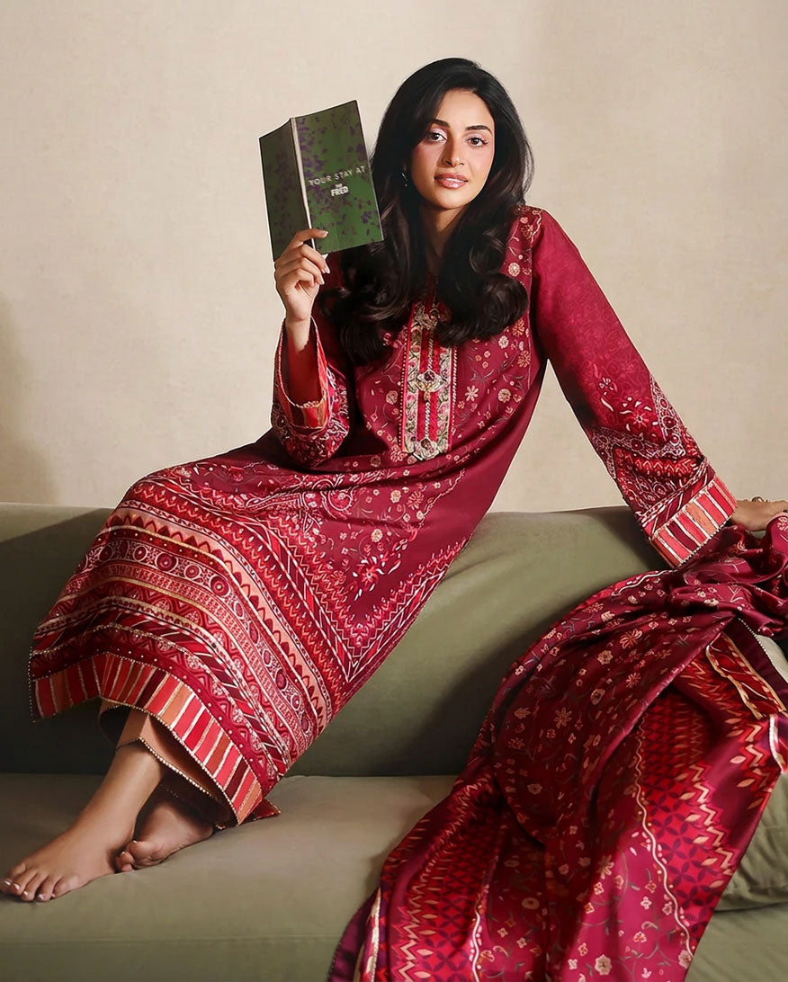 Woman wearing red printed raw silk suit seated on a sofa holding a book