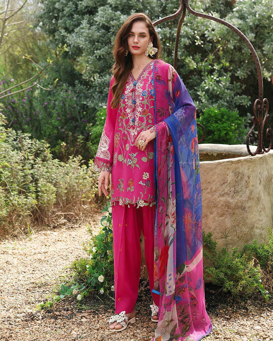 Woman wearing fuchsia unstitched lawn collection suit with floral embroidery, standing near stone well, Secret Garden collection