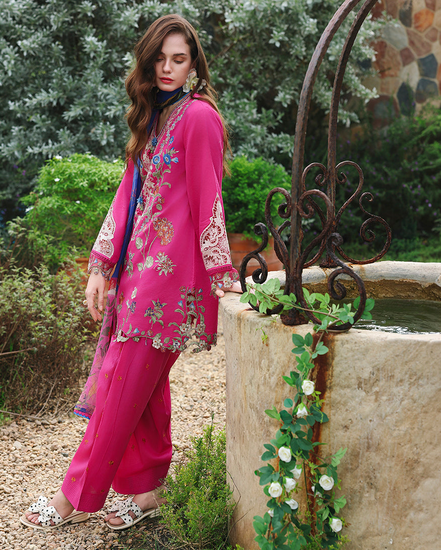 Side view of fuchsia embroidered lawn unstitched suit with lace sleeve detail, standing near stone water basin, Secret Garden collection