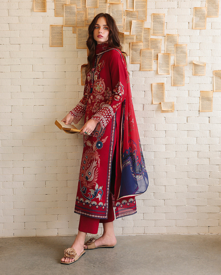 Side view of red unstitched lawn collection suit with paisley embroidery and navy dupatta drape, holding a book, Secret Garden collection
