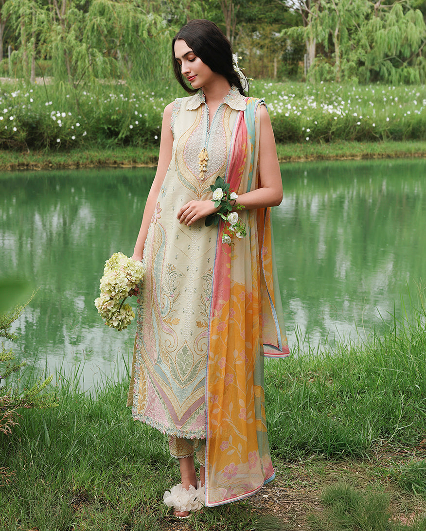 Woman standing by lake wearing lemon yellow unstitched lawn suit with multicolor embroidery, holding flower bouquet, Secret Garden collection